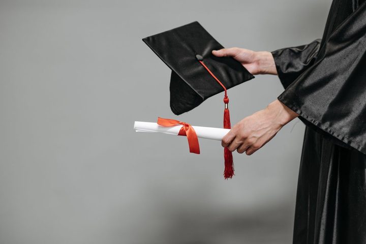 A graduation cap and rolled diploma held in hand